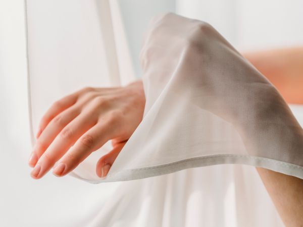 レースのカーテンに触れる女性の手