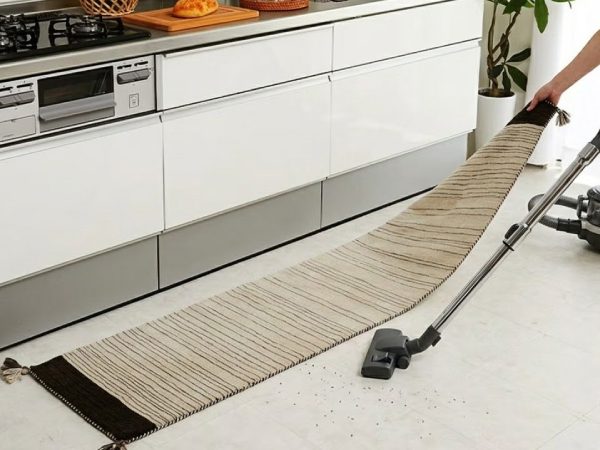 キッチンマットの裏を掃除機掛けする女性